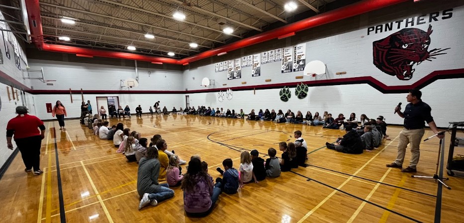 students and teachers sitting in a circle in a school gym